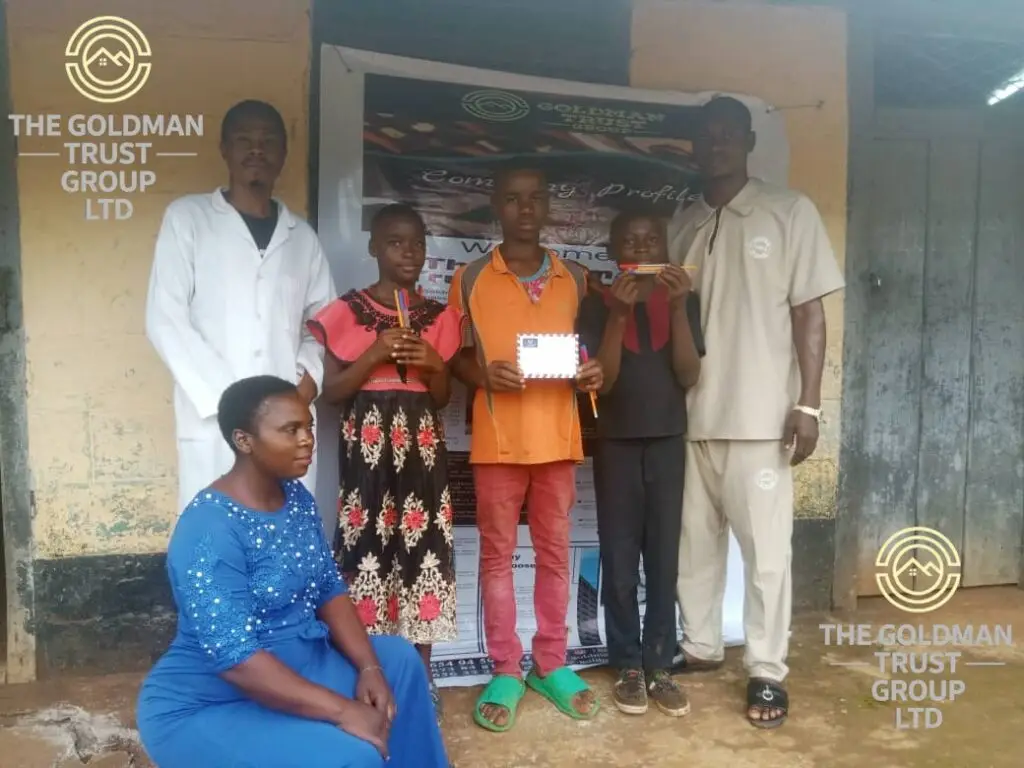 Goldman Trust Group team presenting boxes of pens, chalk, pencils, and papers to a school representative in Ndian Division.