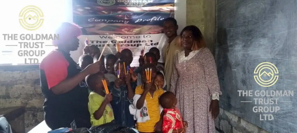 Goldman Trust Group team presenting boxes of pens, chalk, pencils, and papers to a school representative in Ndian Division.
